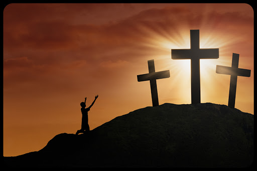 Christian worshiper is sitting on the hill beside the cross on sunset background &#8211; shutterstock_127472144 &#8211; fr