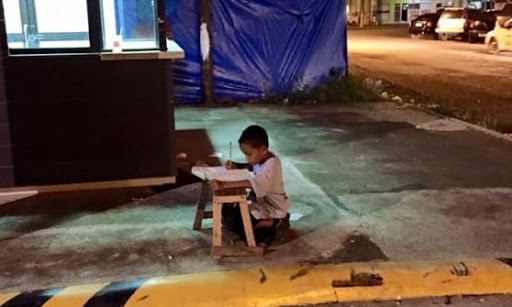 Enfant qui fait ses devoirs dans la rue