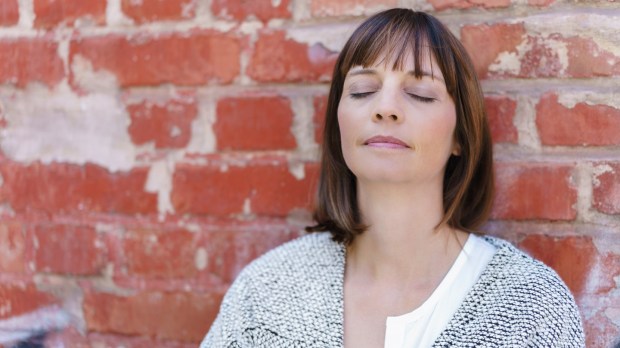 Close up Thoughtful Woman Leaning Against Old Brick Wall with Eyes Closed.