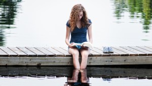 TEENAGER READING A BOOK NEAR A LAKE
