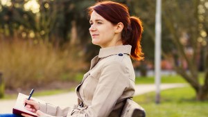 JEUNE FEMME ECRIVANT DANS UN PARC