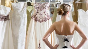 Dziewczyna przymierza suknię ślubne w showroomie i patrzy na wieszak z innymi sukniami.
