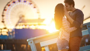 romantic couple kissing at sunset in front of santa monica ferris wheel.