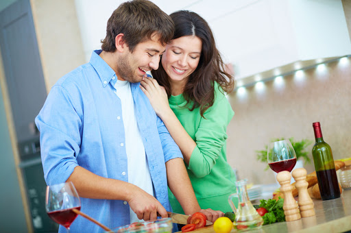 Man cooking salad and his wife embracing him in the kitchen – es
