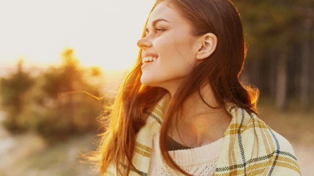 Happy woman near the forest in nature in warm clothes at sunset