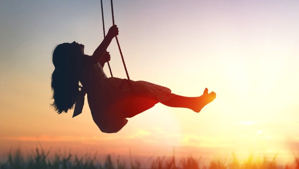 Happy laughing child girl on swing in sunset summer