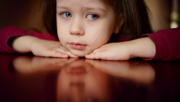 dziewczynka ze smutną miną opiera się na stole