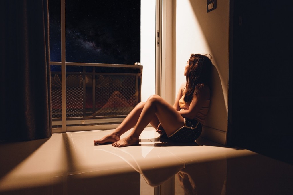 Sad woman sitting on floor looking out window