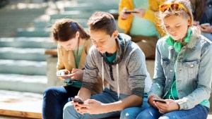 grupa nastolatków siedzi na schodach i wpatruje się w smartfony