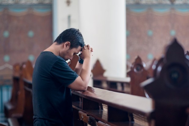 mężczyzna modli się samotnie w kościelnej ławce