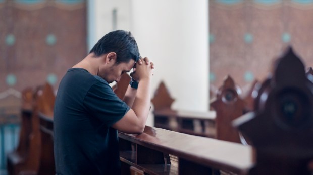 mężczyzna modli się samotnie w kościelnej ławce