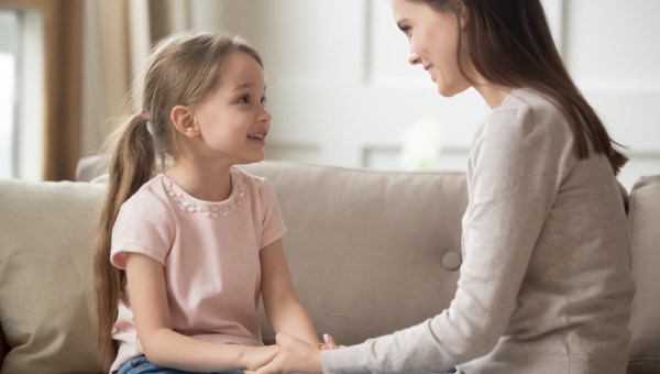 Loving family happy mother and cute child girl holding hands talking sitting on sofa at home