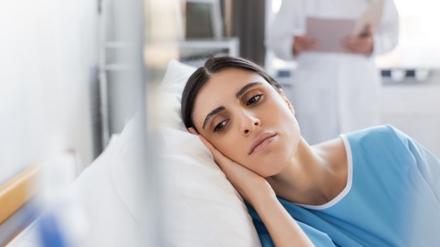 Paciente insatisfecho tumbado en la cama cerca de un médico borroso en la sala del hospital shutterstock_2247559525