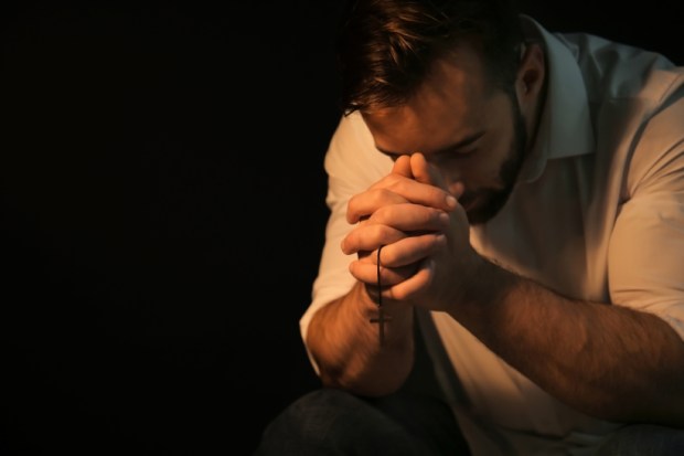 Religious young man praying to God on black background