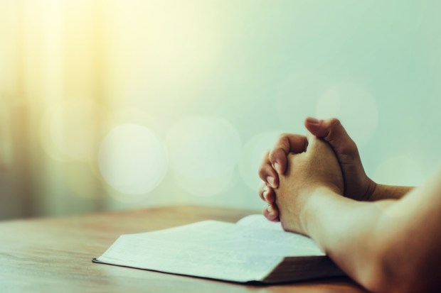 A man praying over bible on wooden table with window and bokeh light, open bible with blurred page, copy space