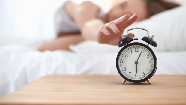 Young sleeping woman and alarm clock in bedroom at home