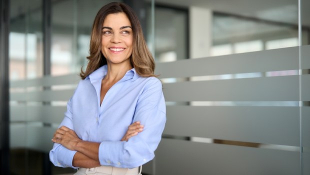 Happy confident mature professional business woman standing at work in office arms crossed looking away