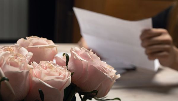 Lettre en papier, photo à la main d'homme, mise au point sur le bouquet de fleurs de rose rose. Lecture d'un message d'amour romantique manuscrit. Correspondance, mémoire manuscrite, courrier électronique et communication