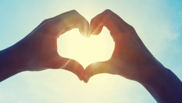 Female hands in the form of heart against the sky pass sun beams