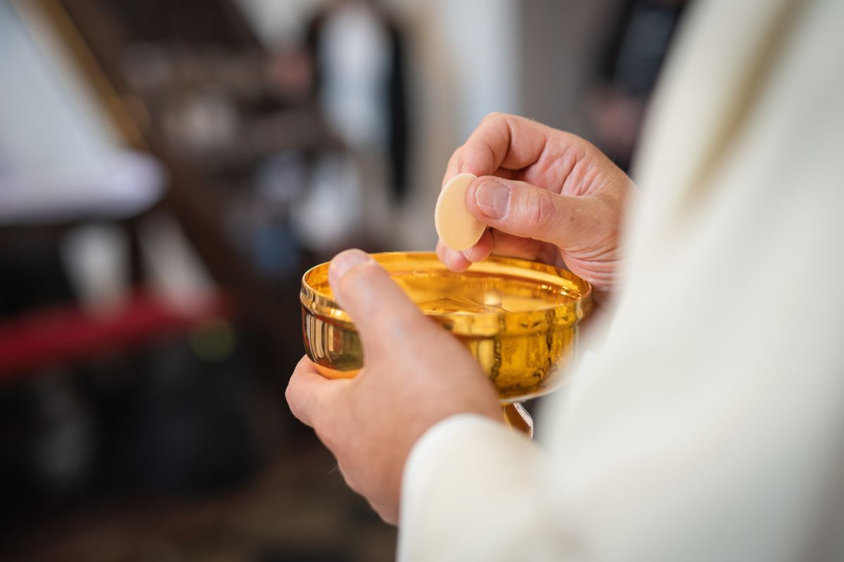 A priest holding a golden chalice and a wafer in his hands while distributing Holy Communion in Poland