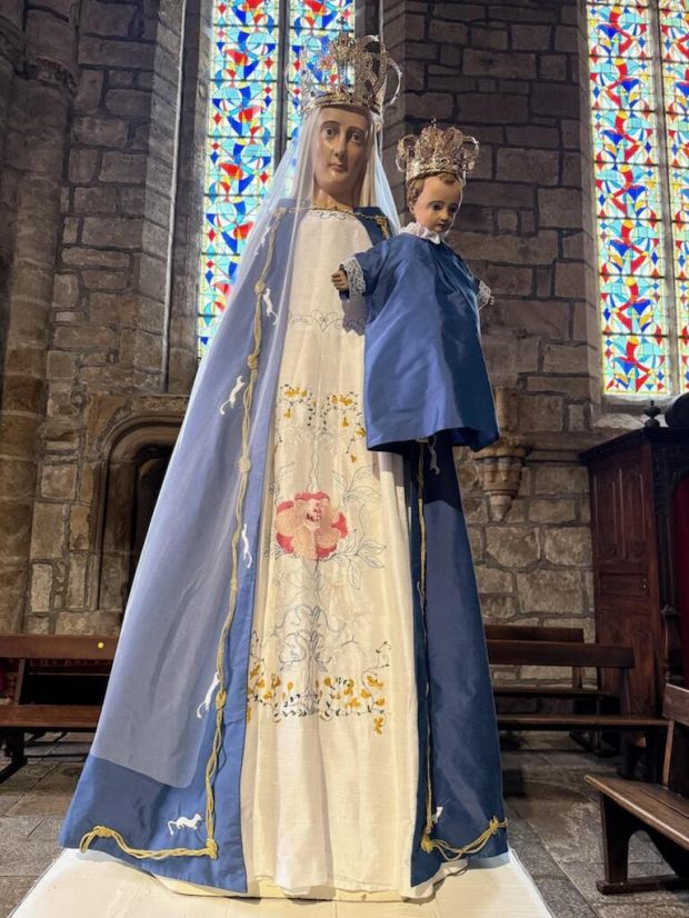 Une hermine, symbole de la Bretagne, court autour des cordes. Sur la robe, des arabesques brodées évoquent un arbre de vie. Au centre, une fleur de camélia et des genêts disent la ville de Guingamp.